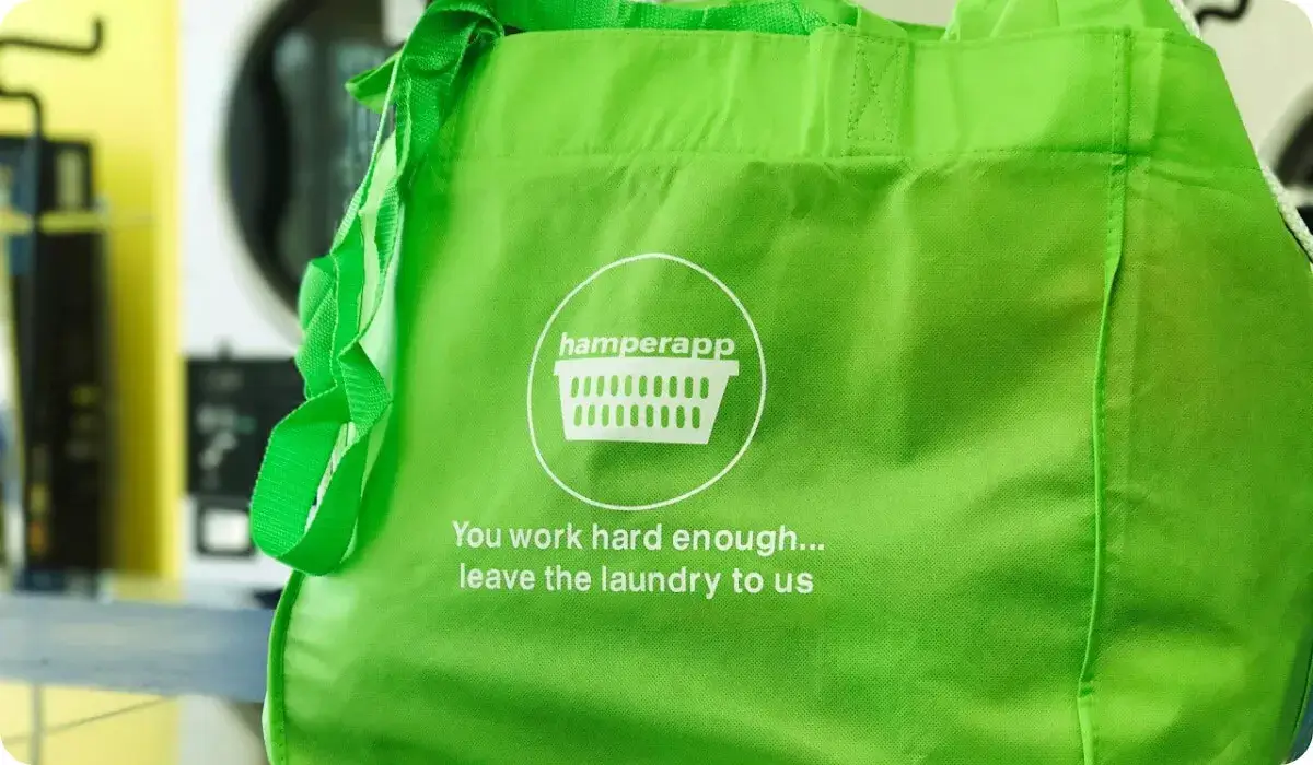 A green Hamperapp laundry bag in front of the washers at a partner laundromat